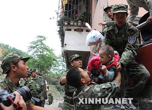 5月13日，在震后的北川縣城，武警戰(zhàn)士將一名和家人失散的幼童救出。 記者從四川省綿陽(yáng)市抗震救災(zāi)指揮部了解到，受災(zāi)特別嚴(yán)重的北川縣老縣城80%、新縣城60%以上的建筑物因地震垮塌，縣城周邊發(fā)生大面積山體滑坡。